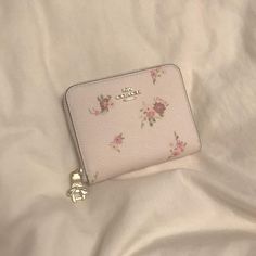 a white purse with pink flowers on it sitting on a bed next to a teddy bear