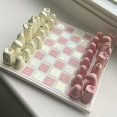 a pink and white checkerboard board with small plastic elephants on it, sitting next to a window sill