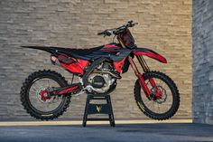 a red and black dirt bike parked in front of a brick wall on a stand