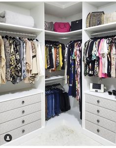 an organized closet with white drawers and clothes hanging on the shelves, all in different colors