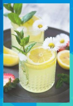 two glasses filled with lemonade and strawberries on a black plate next to flowers