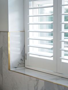 a bathroom with marble counter tops and white shutters