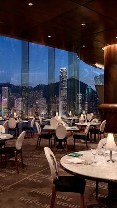 a restaurant with tables and chairs in front of large windows overlooking the city at night