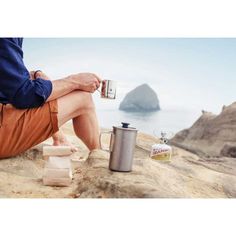 a man sitting on top of a rock next to a cup and some food in front of him