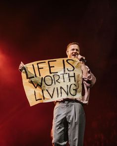 a man standing on stage holding a sign that says life is worth living in front of him