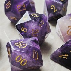 purple dice with gold numbers on them sitting on a table next to some other dice