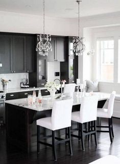 a large kitchen with black cabinets and white chairs in the center island is decorated with crystal chandeliers