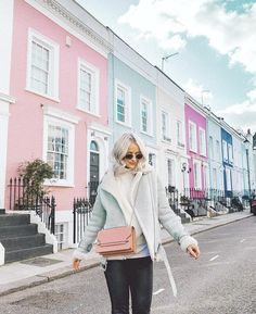 an older woman is walking down the street in front of colorful houses with her hand on her hip