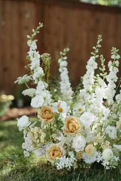 a bouquet of flowers sitting on top of the grass in front of a wooden fence