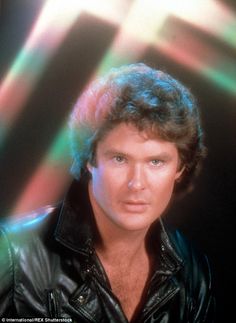 an image of a man in black leather jacket posing for a photo with colored lights behind him