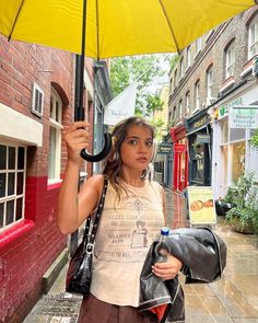 a woman walking down the street with an umbrella over her head and holding a handbag