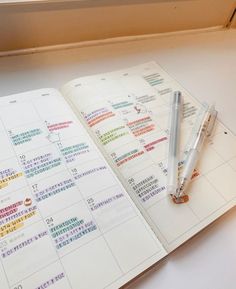 an open planner and pen sitting on top of a white table next to a window