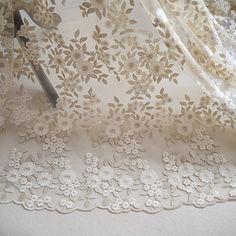 a pair of scissors sitting on top of a white table cloth with floral laces