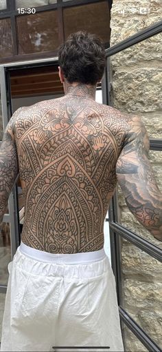 a man with tattoos on his back standing in front of a stone wall and door