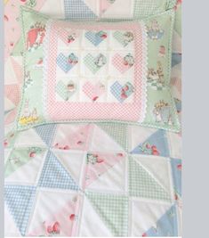 a quilted pillow on top of a bed covered in pink, blue and green