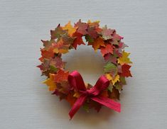 a wreath made out of autumn leaves with a pink bow on the front and side