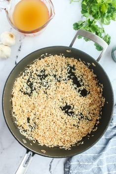 a pan filled with brown rice next to garlic and parsley on a marble counter