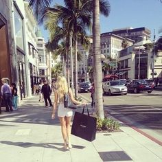 a woman is walking down the street with her suitcase in hand and palm trees lining the sidewalk