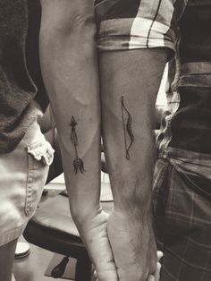 two people holding hands with tattoos on their arms and the other one has an arrow