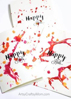 three handmade cards with happy holi written in black ink and red paint splattered on them