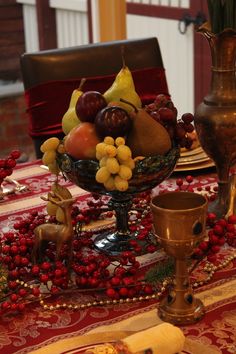 a table topped with a bowl of fruit next to a vase filled with grapes and pears