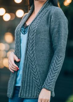 a woman is wearing a gray cardigan sweater and blue jeans with her hand on her hip