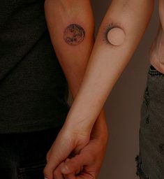 two people holding hands with tattoos on their arms and one has a small moon in the middle