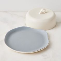 two plates sitting next to each other on a white counter top with a round container in the background