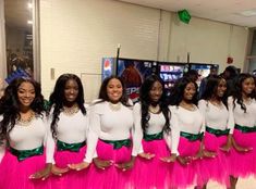 a group of women in pink and green skirts standing next to each other with their hands on their hips