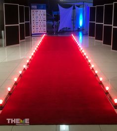 a red carpet with candles on it in front of a white wall and blue lights