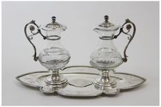 two silver candlesticks sitting on top of a metal tray with an ornate design