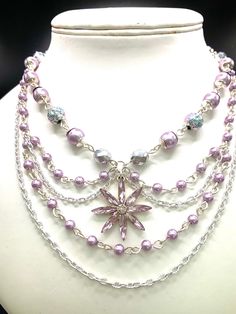 a white mannequin with purple beads and a silver flower on the front necklace