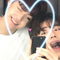 two young men looking at their cell phones in front of a heart - shaped frame