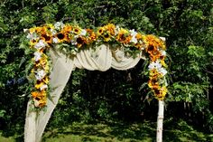 an outdoor wedding arch decorated with sunflowers and greenery