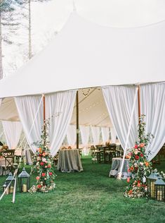 an outdoor tent set up with white drapes and flowers on the grass for a wedding reception