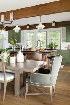 a kitchen with green cabinets and white chairs in front of a table that has two vases on it