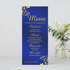 a blue and gold menu card sitting next to a vase with white flowers on it