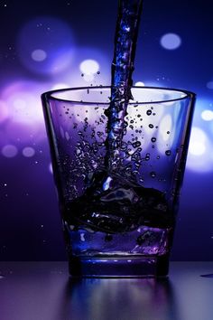 water being poured into a glass with ice cubes on the table next to it