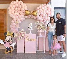 a man and woman standing next to a baby girl in front of a minnie mouse balloon arch