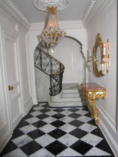 an ornate staircase with black and white checkered flooring, chandelier and mirror