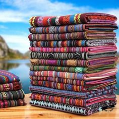 a stack of colorful fabrics sitting on top of a wooden table next to a lake