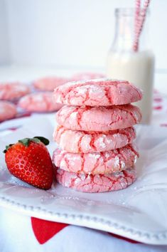 a stack of pink powdered sugar cookies next to a strawberry on a white plate