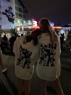 two people standing in the street at night with their backs to each other, wearing hoodies that have photos on them