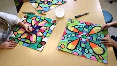 two children sitting at a table working on stained glass art projects with crayons