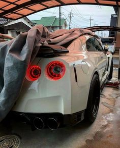 the back end of a white sports car covered with a tarp in a garage