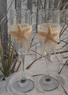 two wine glasses with starfish decorations on them sitting in the sand near some plants