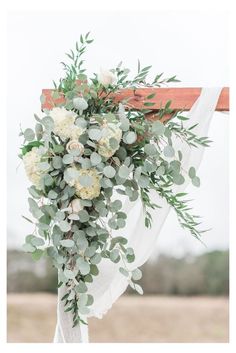 a bouquet of flowers and greenery is hanging from a wooden cross at the end of a wedding ceremony