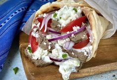 a pita filled with meat and vegetables on a cutting board next to a blue towel