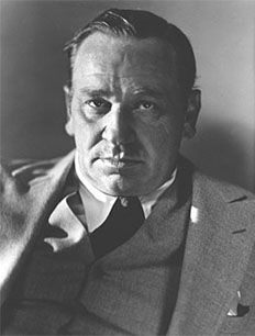 an old black and white photo of a man in a suit with his hand up