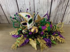 a mardi gras mask with purple, green and gold decorations sits on a wooden surface